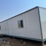 A portable modular cabin designed for construction sites, featuring a robust metal frame, large windows, and a durable roof structure
